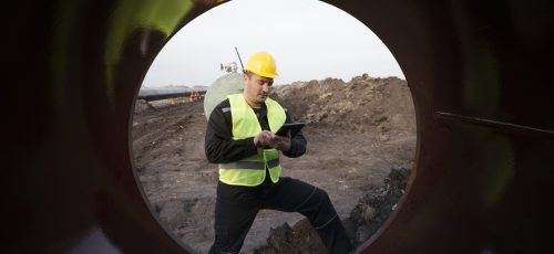 Shot of an oilfield worker checking quality of gas pipes at construction site.