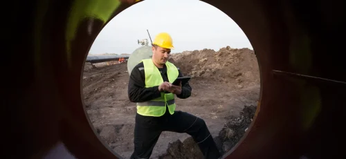 Shot of an oilfield worker checking quality of gas pipes at construction site.